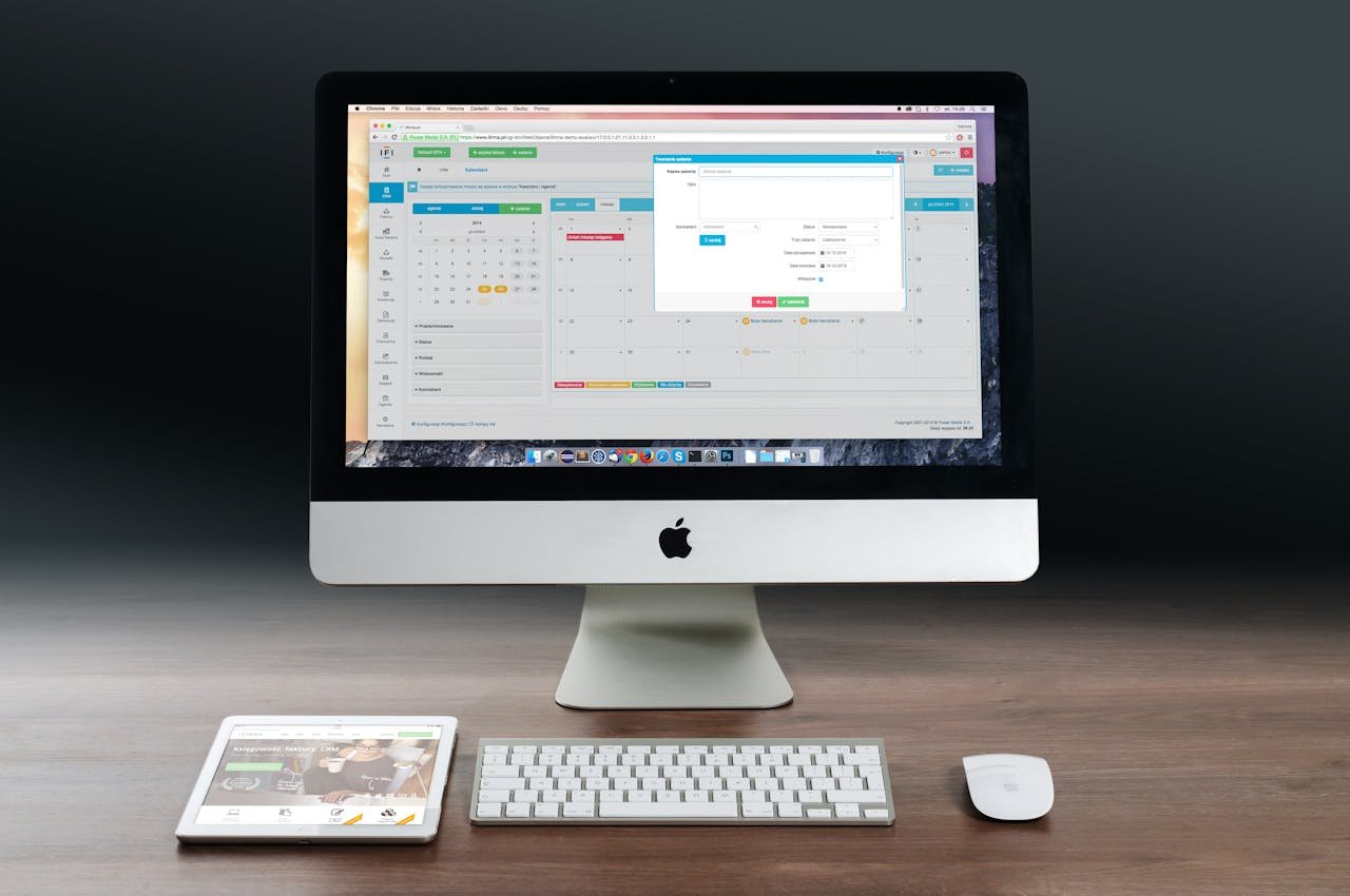 contact-img A sleek office setup featuring an Apple iMac, iPad, and keyboard on a wooden desk.