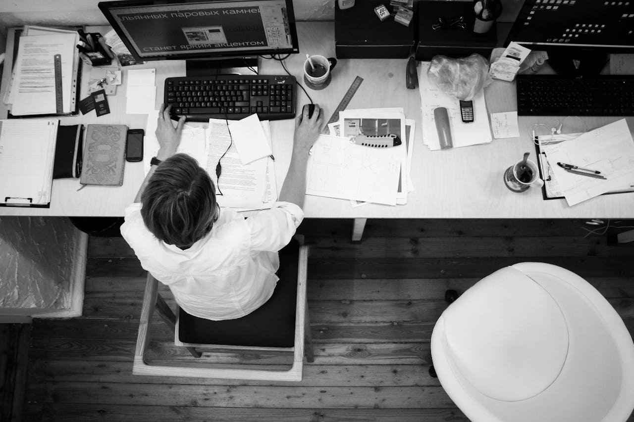 services-01 Black and white image of an employee working at a desk with papers and computer.