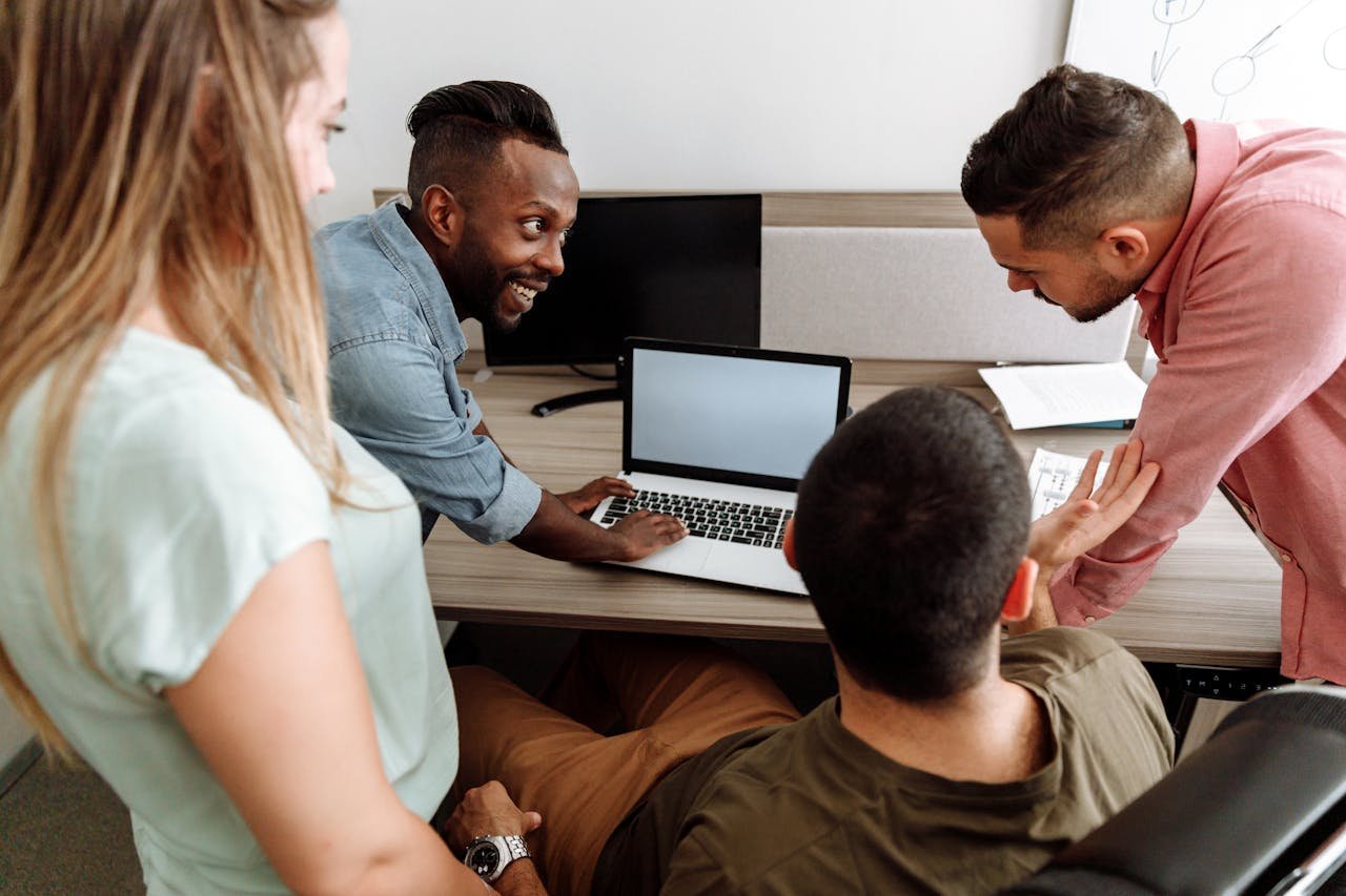 our-experience Four colleagues brainstorming around a laptop in a bright, modern office setting.