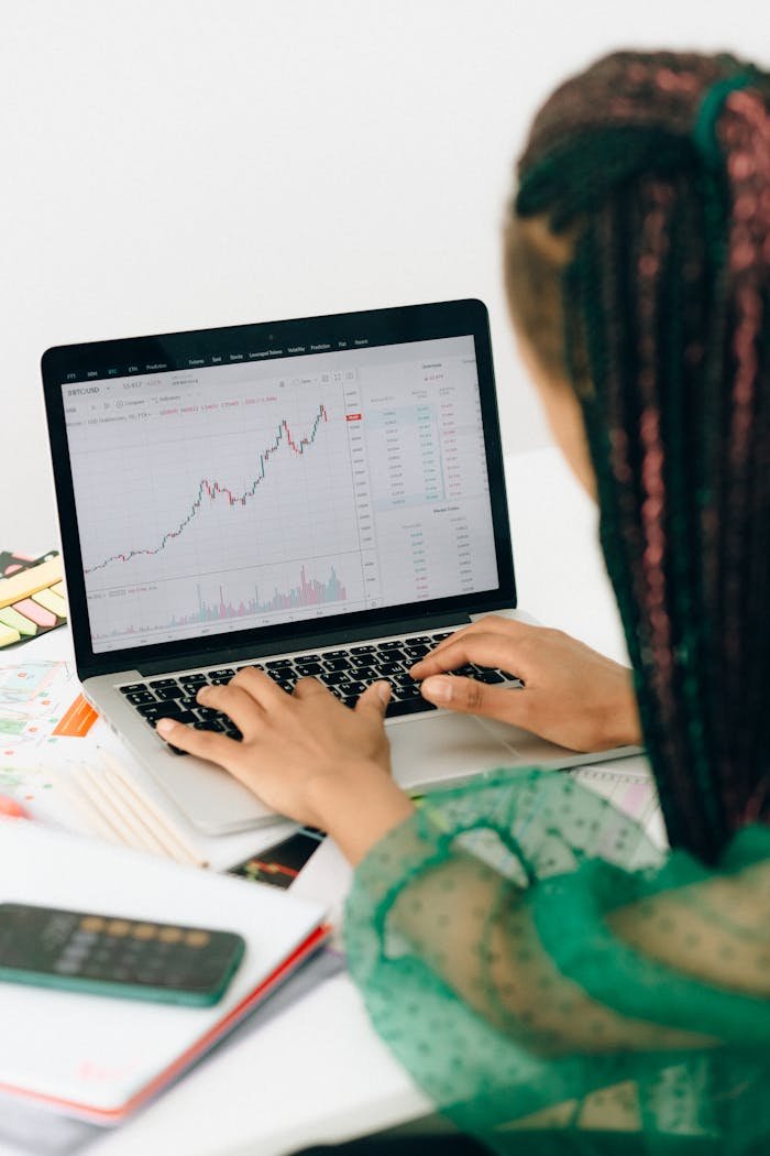gallery-1 A woman working on financial analysis using a laptop with a stock market graph on screen.